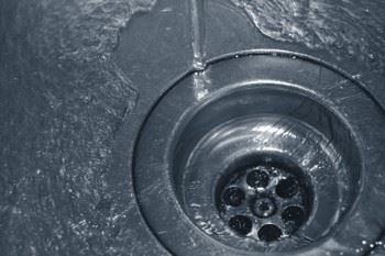 Close-up view of a metal sink drain with water droplets on the surface.