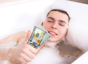 Person in a bubble bath holding a stack of U.S. hundred-dollar bills, smiling with closed eyes.