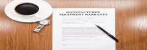 A warranty document is on a wooden desk with a pen, a wristwatch, and a cup of black coffee on a saucer.