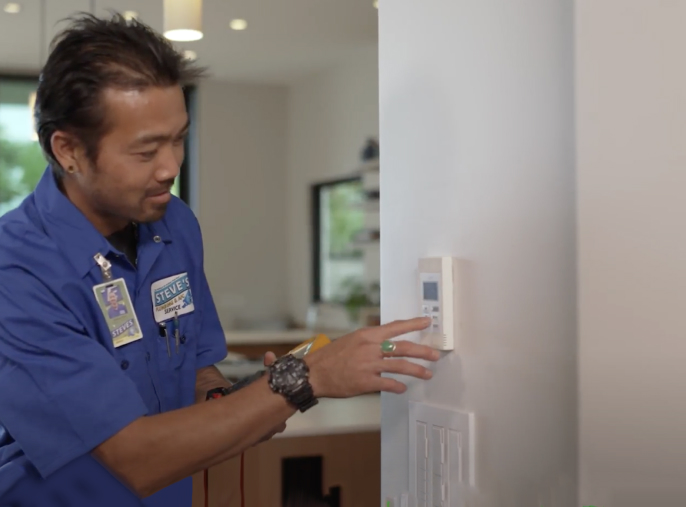 A person wearing a blue uniform adjusts a wall-mounted thermostat in a modern room.