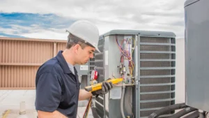 Technician in a hard hat inspects and tests an outdoor HVAC unit with a multimeter.