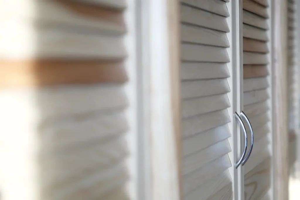 Close-up of louvered wooden wardrobe doors with metal handles.