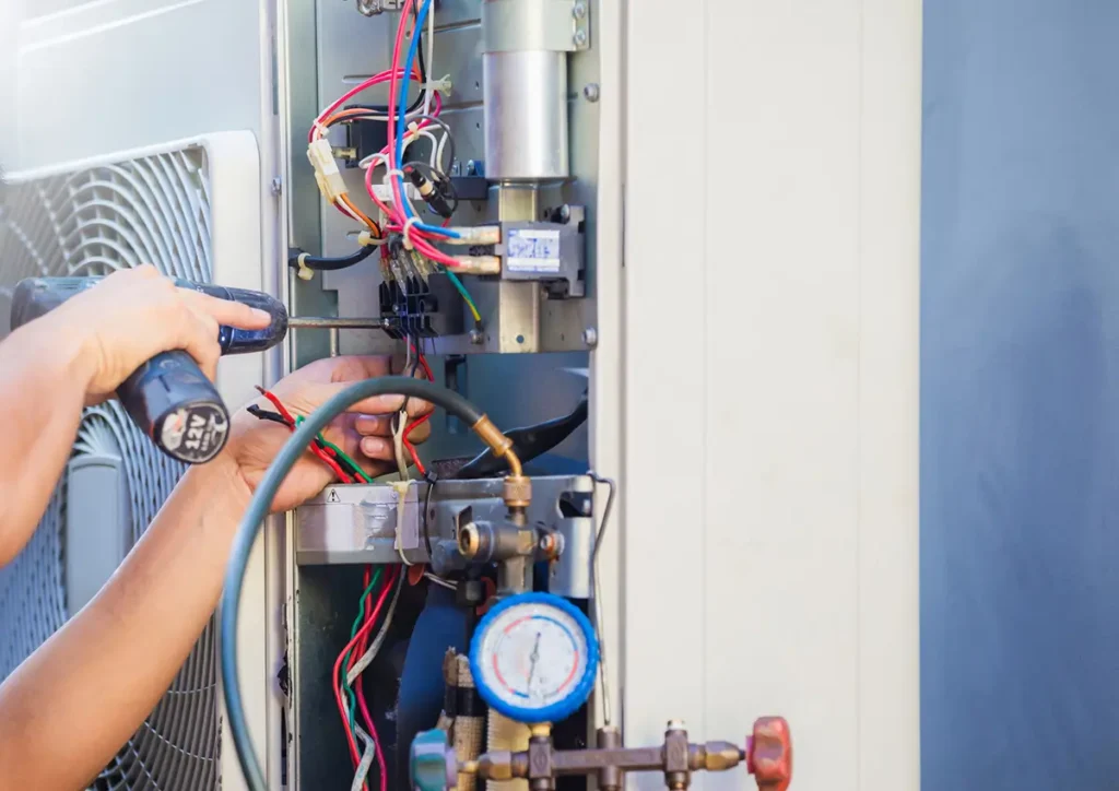 A technician uses a screwdriver to service an HVAC unit, surrounded by colorful wires and a pressure gauge.