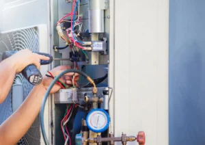 A technician uses a screwdriver to service an HVAC unit, surrounded by colorful wires and a pressure gauge.