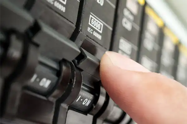 Close-up of a finger turning on a circuit breaker switch labeled "ON" and "6000 IEC 609".