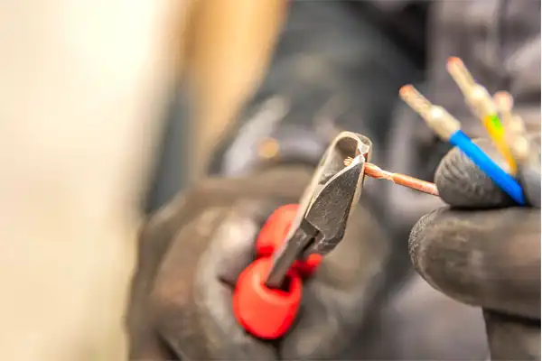 A person wearing gloves uses red-handled pliers to strip the insulation from a group of colored electrical wires.